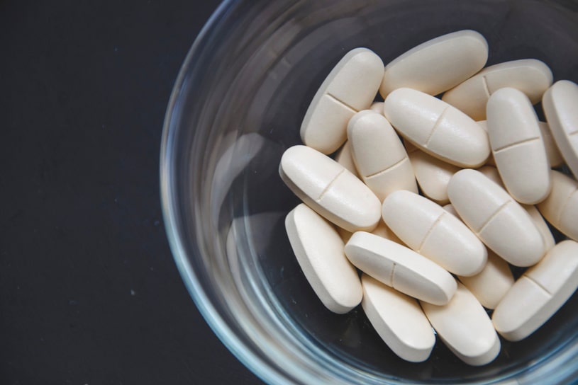 White Ambien pills in a transparent glass on a black background.