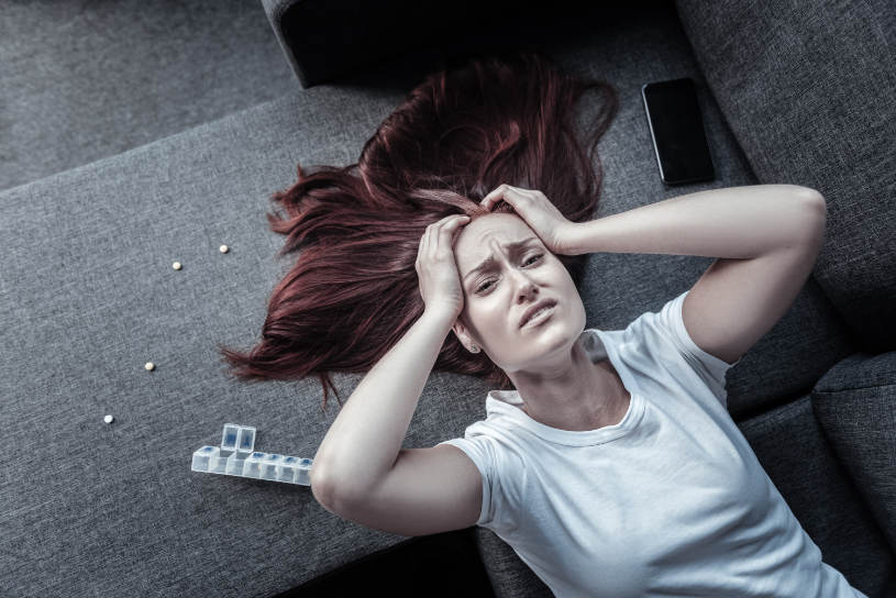 A depressed woman lies in bed and holds her head.