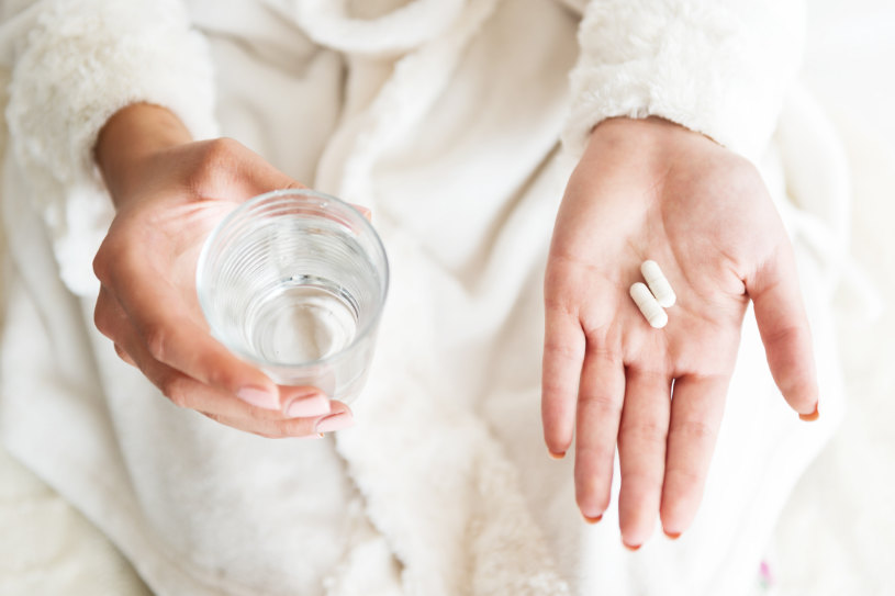 A woman holds some pills in one hand and a glass of water in the other.