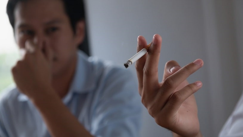Woman smoking at home and man covering his nose.