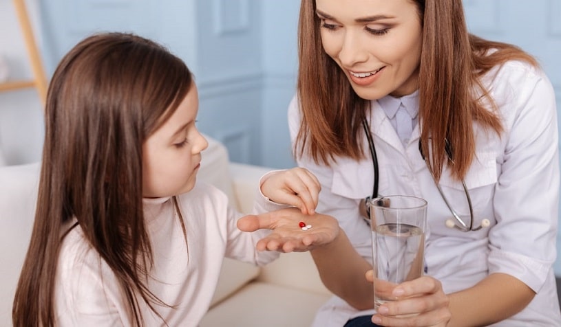 Nurse giving pills to a small girl.