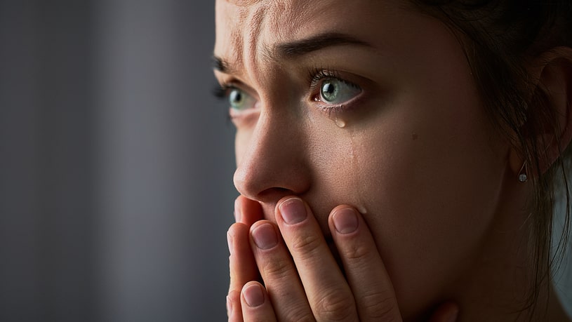 Crying woman with wide-open eyes and covered mouth with hands.