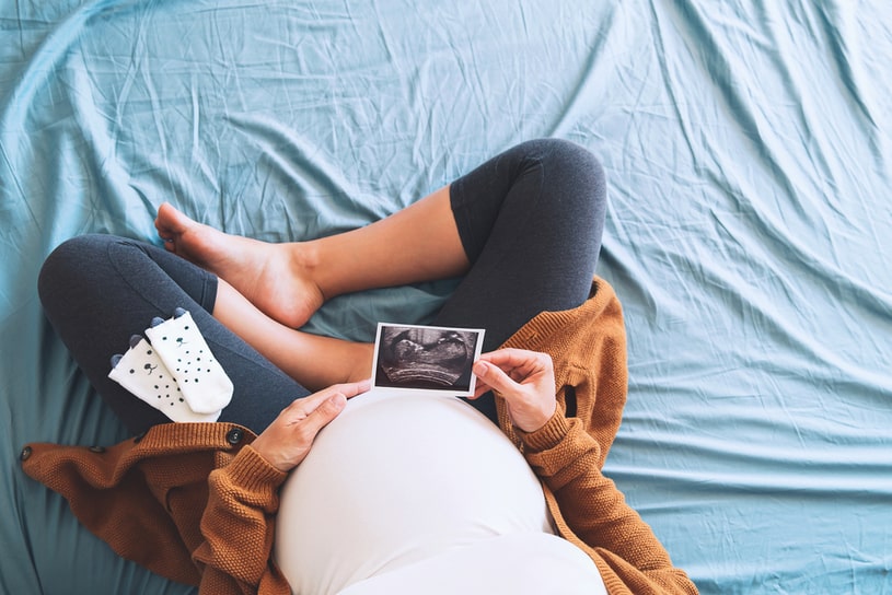 A pregnant woman is sitting with an ultrasound scan.