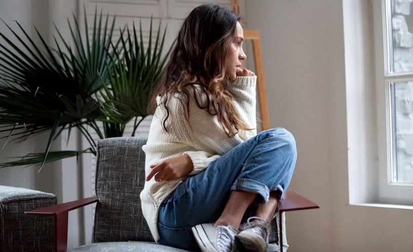 Depressed woman sitting on the chair looking in the window.