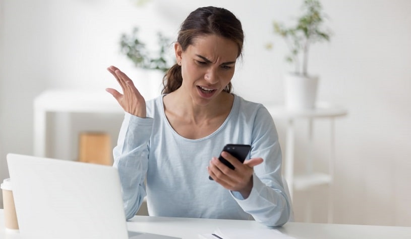 Irritated woman looking at her phone during caffeine withdrawal.
