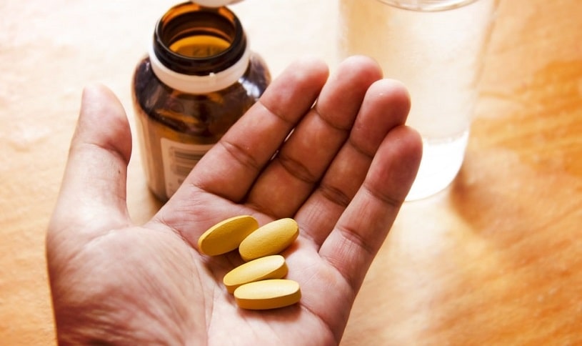Baclofen tablets in hand next to a pill bottle.