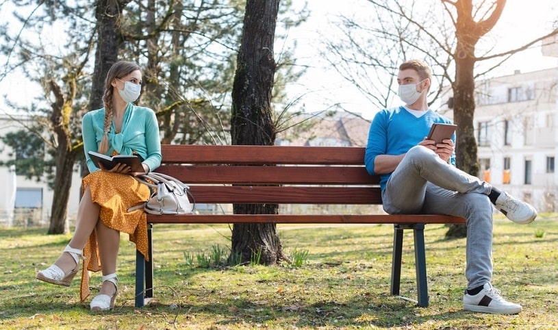 Social distancing: man and woman wearing masks on the benach in the park.