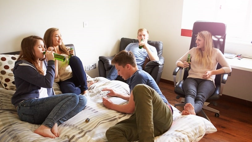Teenages drink alcohol in the bedroom.